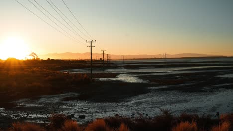 Timelapse-Panorámico-Del-Atardecer-En-Humedales-De-Nueva-Zelanda-Con-Postes-De-Energía-Y-Chimeneas