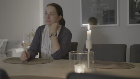 depressed and unhappy young woman sitting at dining table drinking wine