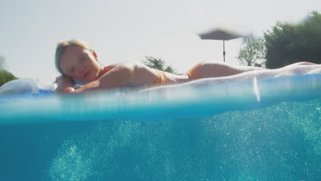 underwater view of man splashing woman floating on airbed in swimming pool on summer holiday