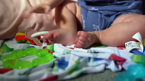 close up of baby feet while infant is playing with rattle, teething ring on blanket