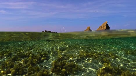 perspectiva de la superficie del agua de mar del velero en el horizonte con velas bajadas entre rocas