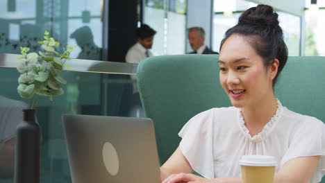 businesswoman using laptop working at table in breakout seating area of office building