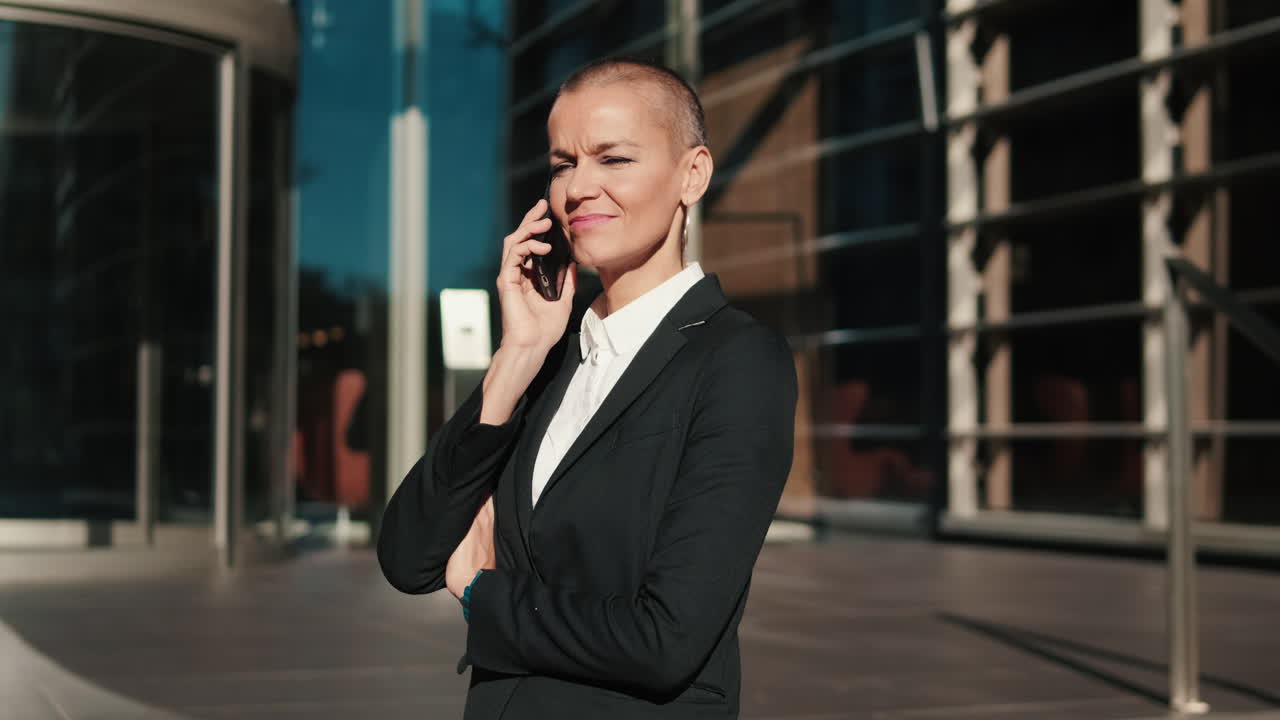 Professionel kvinde, der taler i smartphone udenfor en moderne kontorbygning