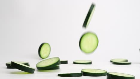 Bright-green-fresh-cucumber-slices-falling,-flipping-and-bouncing-on-white-backdrop-in-slow-motion