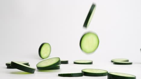 bright green fresh cucumber slices falling, flipping and bouncing on white backdrop in slow motion