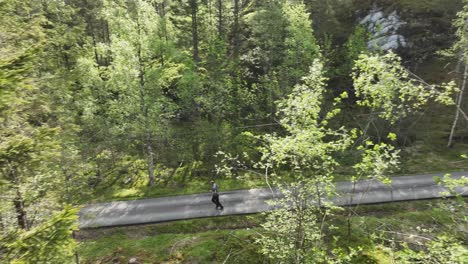Peekaboo-aerial-view-through-branches-of-man-jogging-at-paved-forest-path---60fps