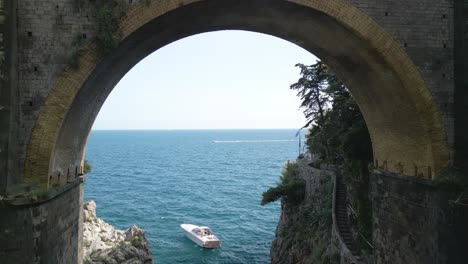 Drone-Flies-Under-Bridge-as-Boat-Anchors-in-Sea-Along-Amalfi-Coast
