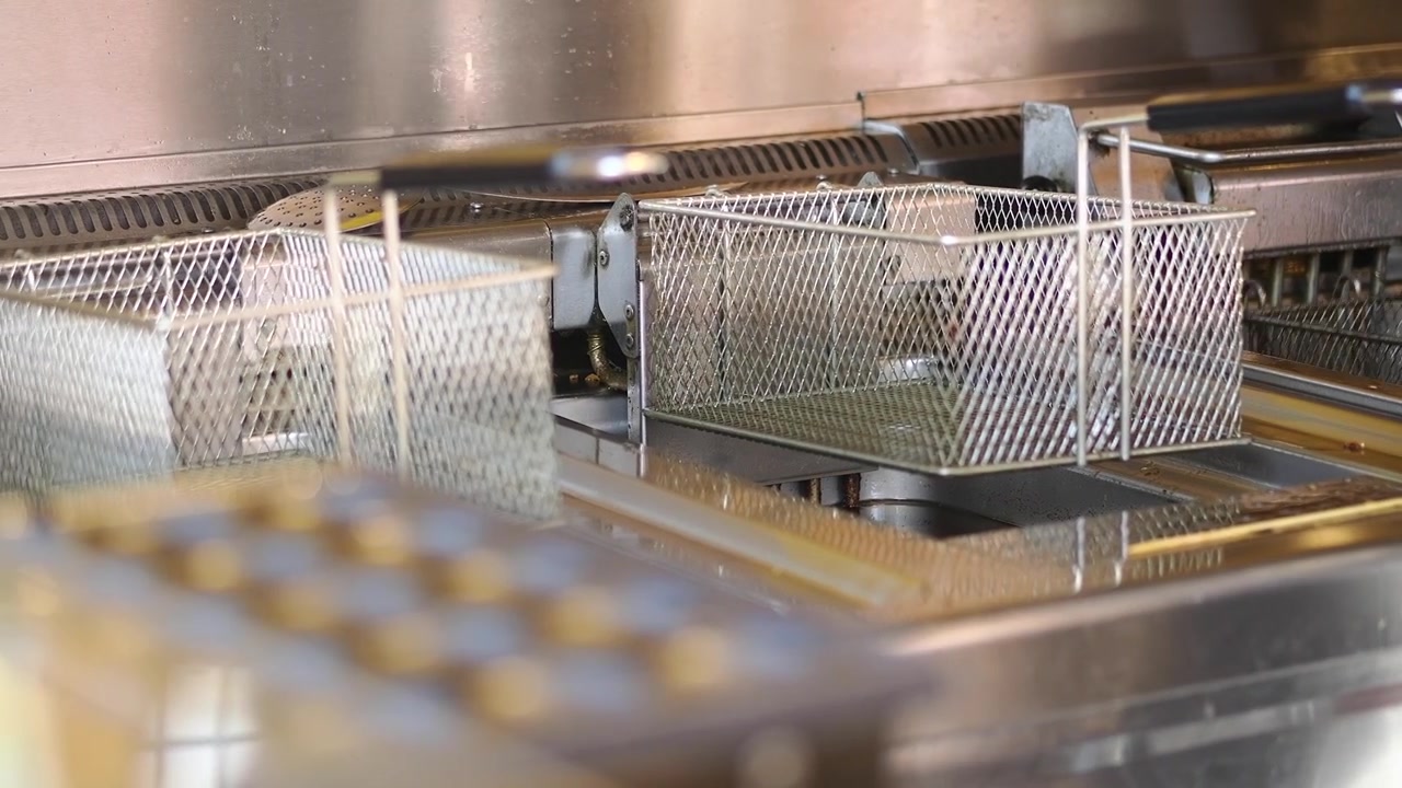 Cestelli vuoti della friggitrice che si sollevano dall'olio caldo in una cucina professionale