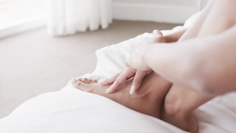 Close-up-of-legs-and-hands-of-biracial-woman-sitting-on-bed-at-home,-slow-motion