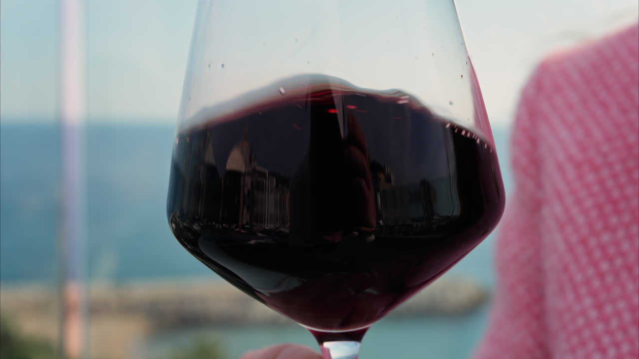Close up of a woman swirling a glass of red wine on a table at a terrace with a sea view