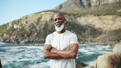 older man with arms crossed stands near the ocean