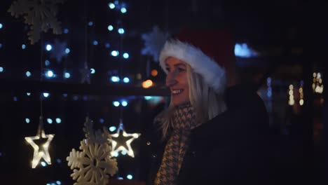 a woman in a santa hat looks at a shop window at night.