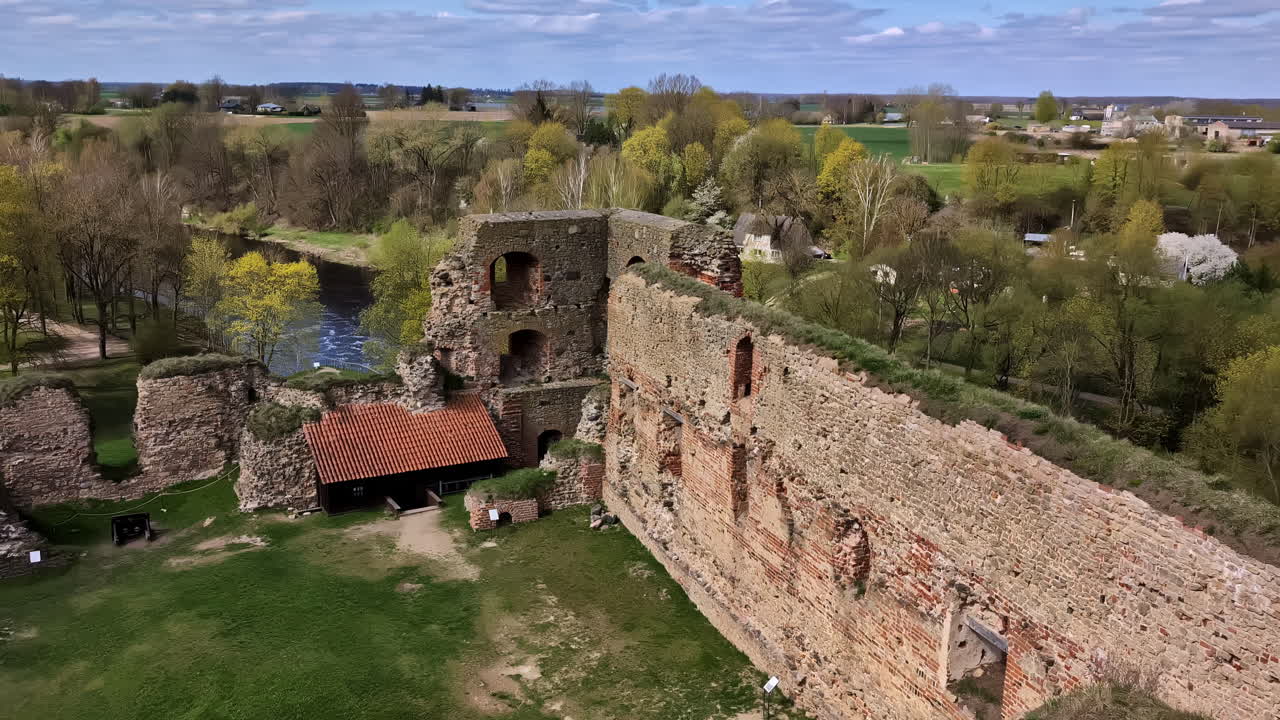 Ripresa a volo d'uccello con drone sopra le rovine di una fortezza medievale circondata da alberi e campi