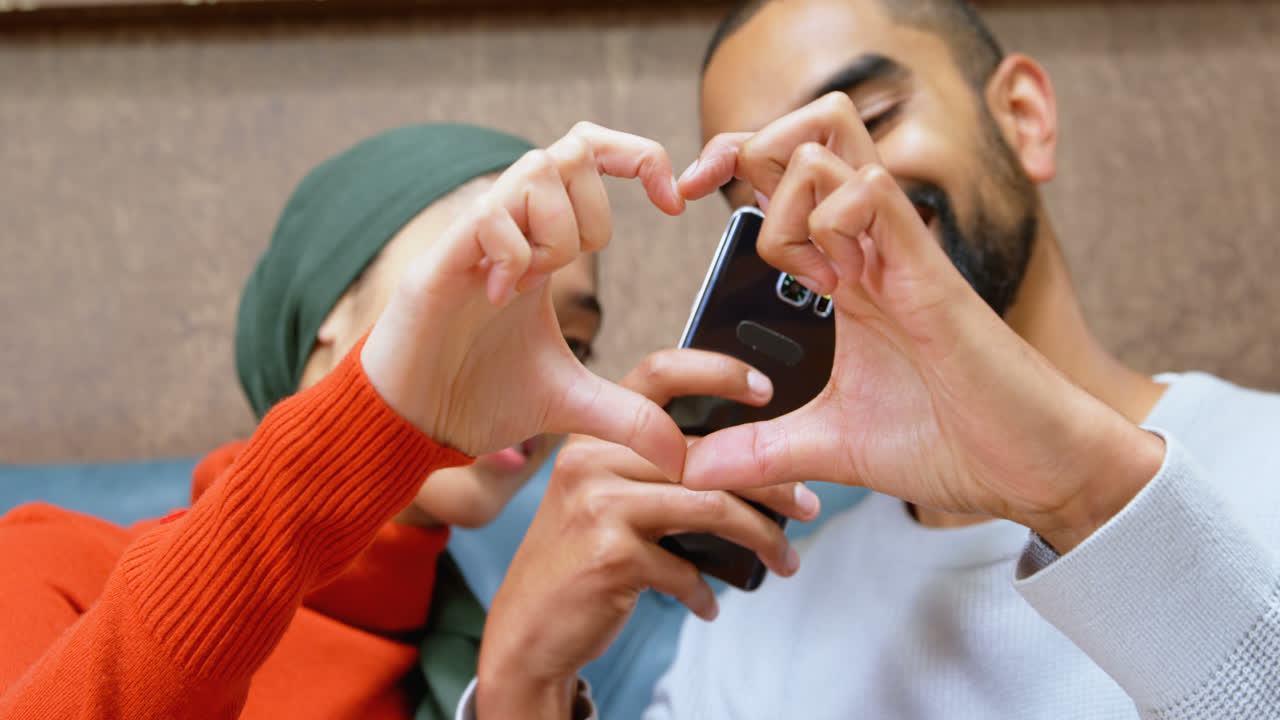 Couple forming heart shape sign while taking photo with mobile phone 4k
