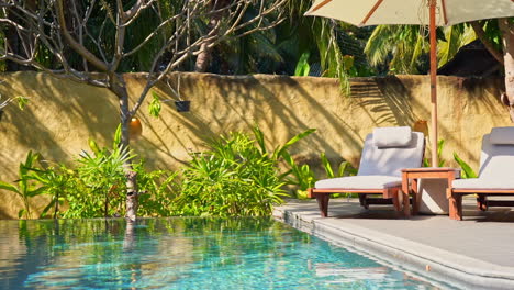 two empty sun loungers sit under a shade umbrella at the edge of an infinity pool