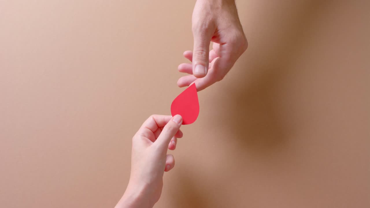 manos de personas caucásicas dando gota de sangre en fondo beige con espacio de copia, cámara lenta