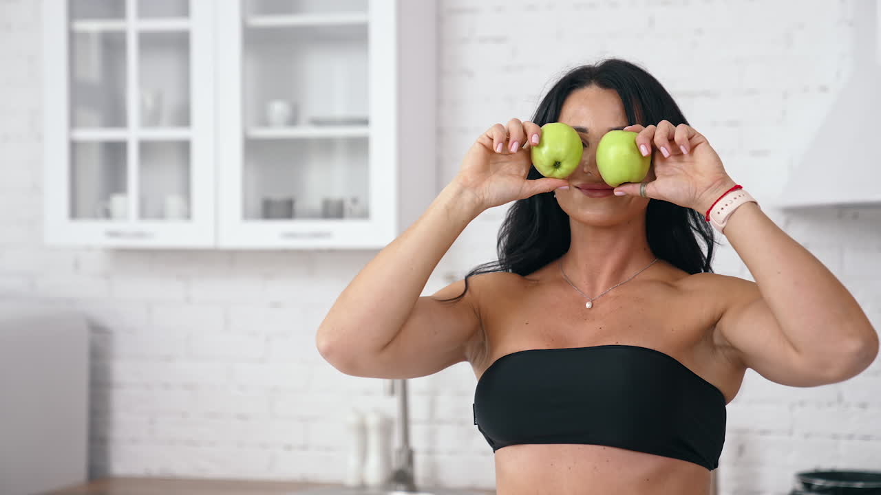 Bella donna caucasica bruna in piedi vicino a un tavolo con mele salutari che gioca con esse. Concetto di cibo sano per la dieta
