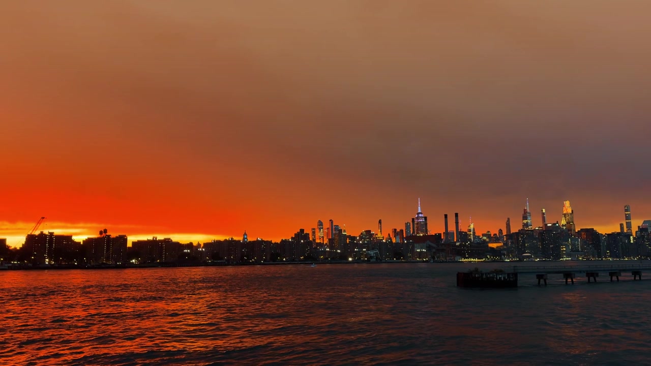 Deep orange air pollution over Manhattan skyline from wildfires. Midtown skyscrapers under thick amber smoke clouds next to east river during climate crisis event.