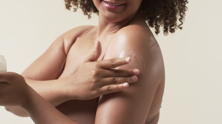 biracial beautiful plus size woman applying lotion to her shoulder, smiling confidently