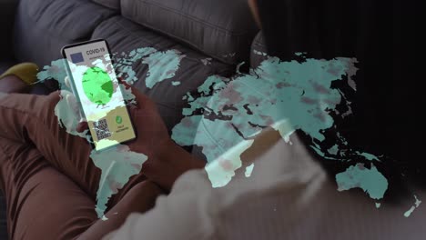 animation of woman holding smartphone with covid 19 vaccination passport over world map