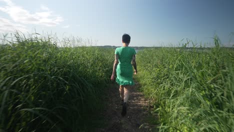 Vista-De-Cardán-De-Una-Mujer-Caminando-Por-Un-Sendero-A-Través-De-La-Hierba-Alta-Al-Lado-Del-Océano