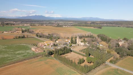 Vista-Aérea-De-La-Naturaleza-Campo-Sembrado-Sin-Gente-Montaña-Nevada-De-Los-Pirineos-En-El-Fondo-Pequeña-Ciudad-En-Cataluña