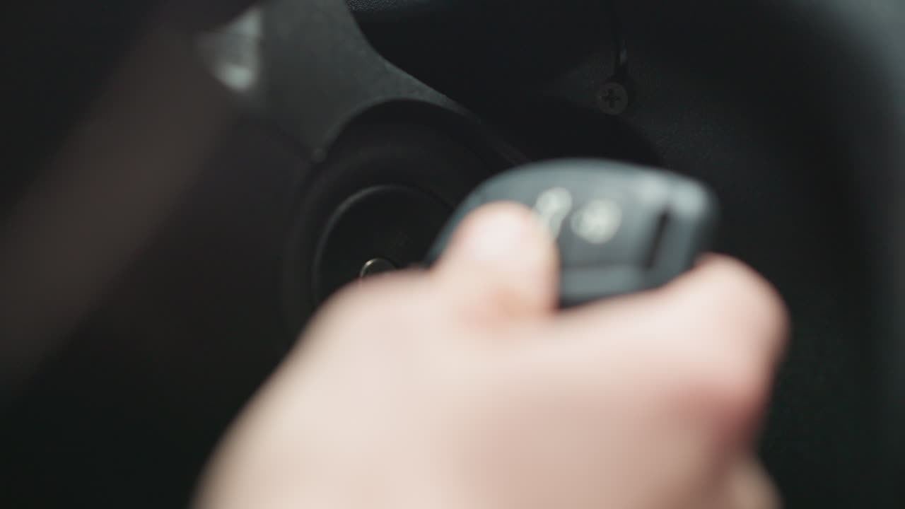 Close up of commuter inserting metal key into ignition starter and turning key inside vehicle cabin focusing on hand movement dashboard detail and jacket sleeve during winter commute preparation