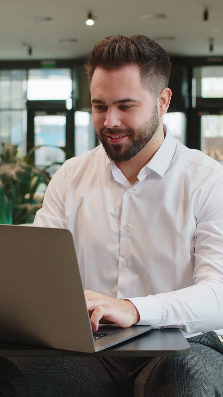 Smiling businessman closing laptop pc computer after finishing work sitting in modern office lobby