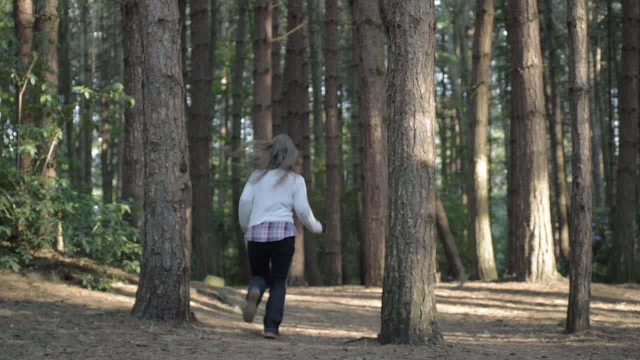 Woman running in empty pine forest with walking stick wide shot
