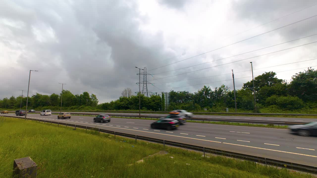 Timelapse Busy Traffic Flowing Along M4 Motorway Dual Carriageway with Roadside Lamps and Electric Pylons and Dark Contrasting Clouds in Sky