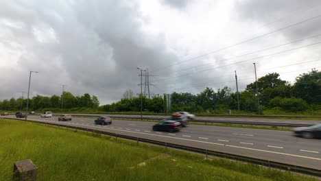 timelapse busy traffic flowing along m4 motorway dual carriageway with roadside lamps and electric pylons and dark contrasting clouds in sky