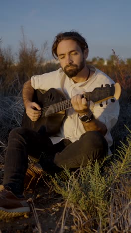 a man playing an acoustic guitar outdoors at sunset