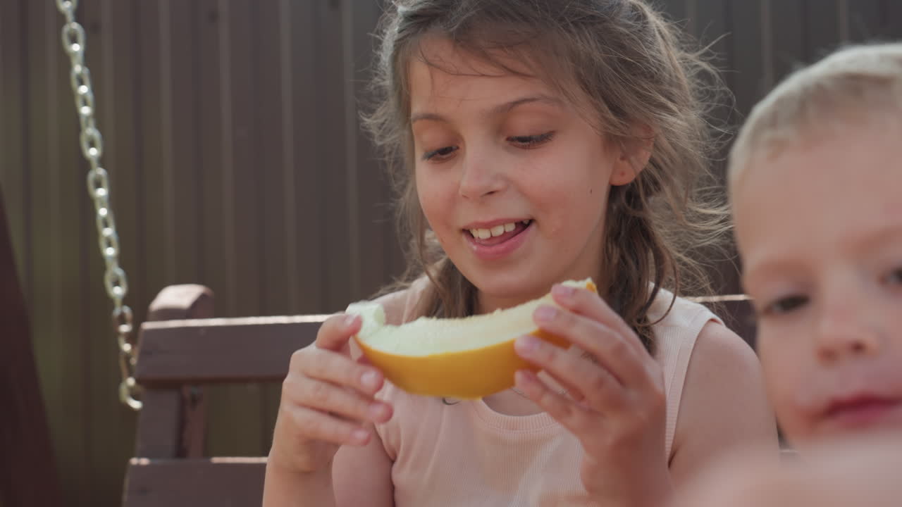 Child Enjoying Sunny Melon Snack, Bright Outdoor Scene With Smiling Child Enjoying Juicy Melon Piece, Sunlit Backyard Setting Featuring Cheerful Girl Savoring Slice Of Fresh Melon During Summer