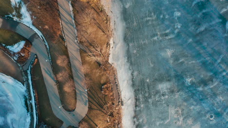 Aerial-shot-of-walking-trails-in-park-alongside-frozen-lake