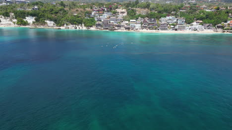 Una-Mantarraya-Nada-En-Primer-Plano-Mientras-Los-Surfistas-Flotan-En-El-Fondo-Frente-A-Uluwatu,-Bali,-Indonesia.