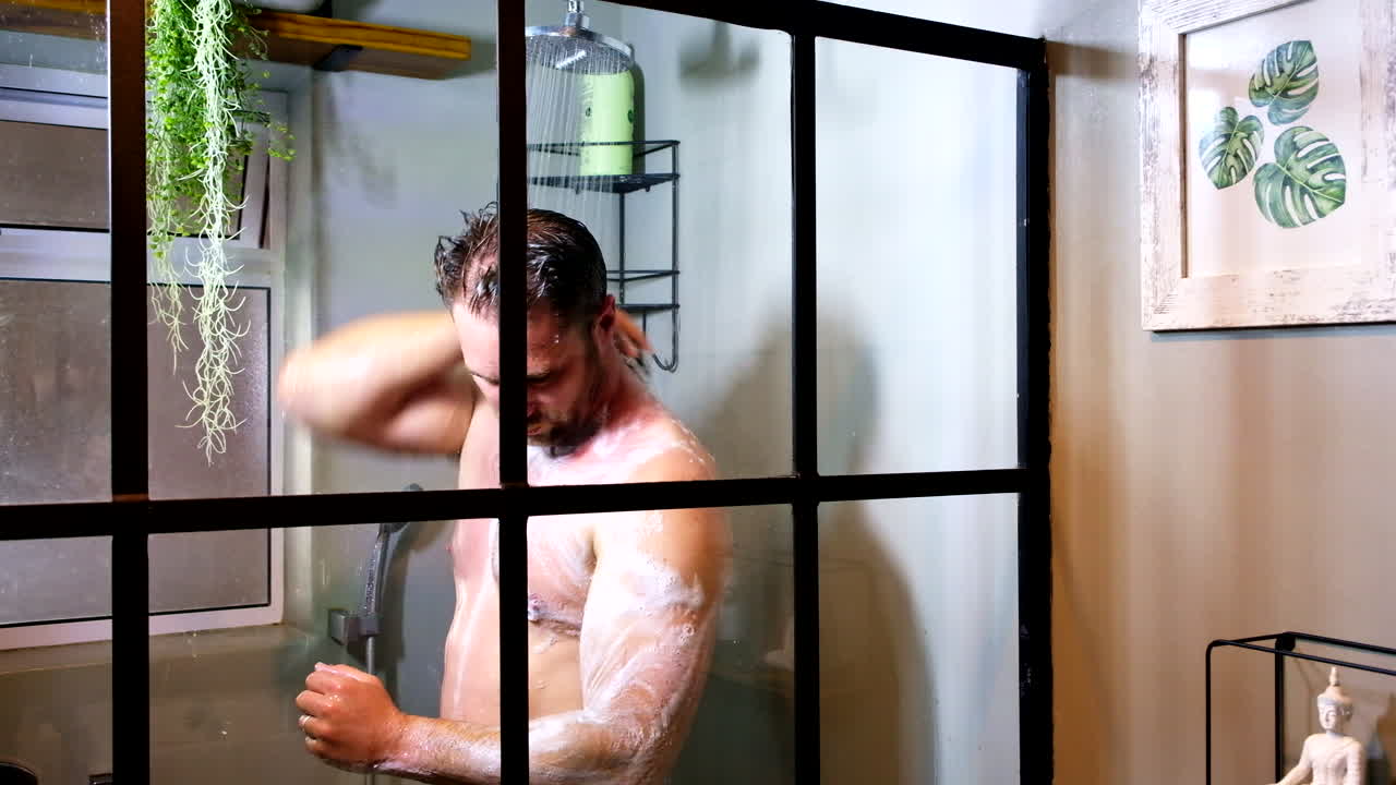 White male washing body with soapy sponge under shower, side view
