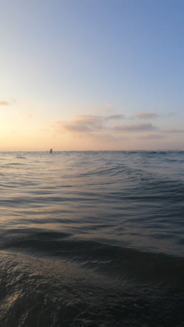 Ein-Wunderschöner-Sonnenuntergang-über-Dem-Meer-Mit-Wellen,-Die-Ans-Ufer-Krachen,-Und-Einem-Schwimmer,-Der-Im-Wasser-Im-Hintergrund-Watet