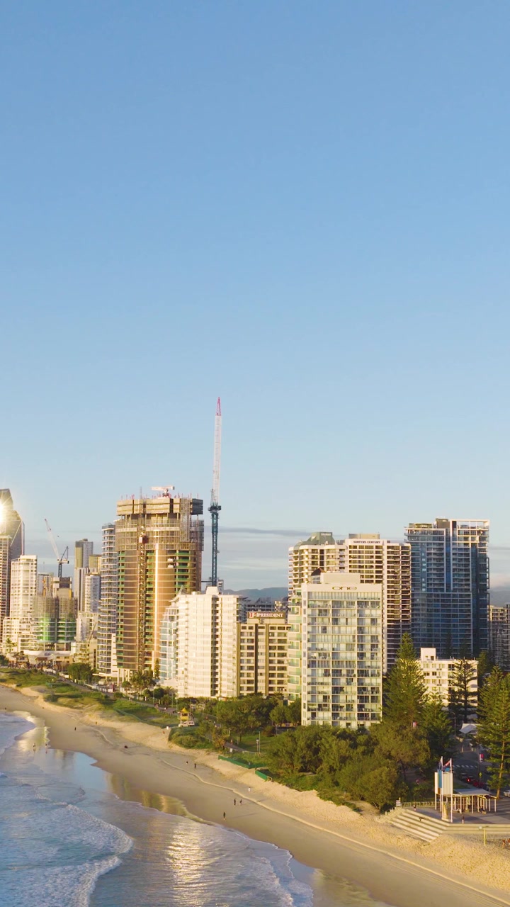 Imagens aéreas capturam o horizonte e a praia da Gold Coast sob céus azuis claros com ondas suaves e uma paisagem urbana vibrante
