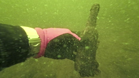 underwater view of severely polluted water with diver's hand holding dirty bottle