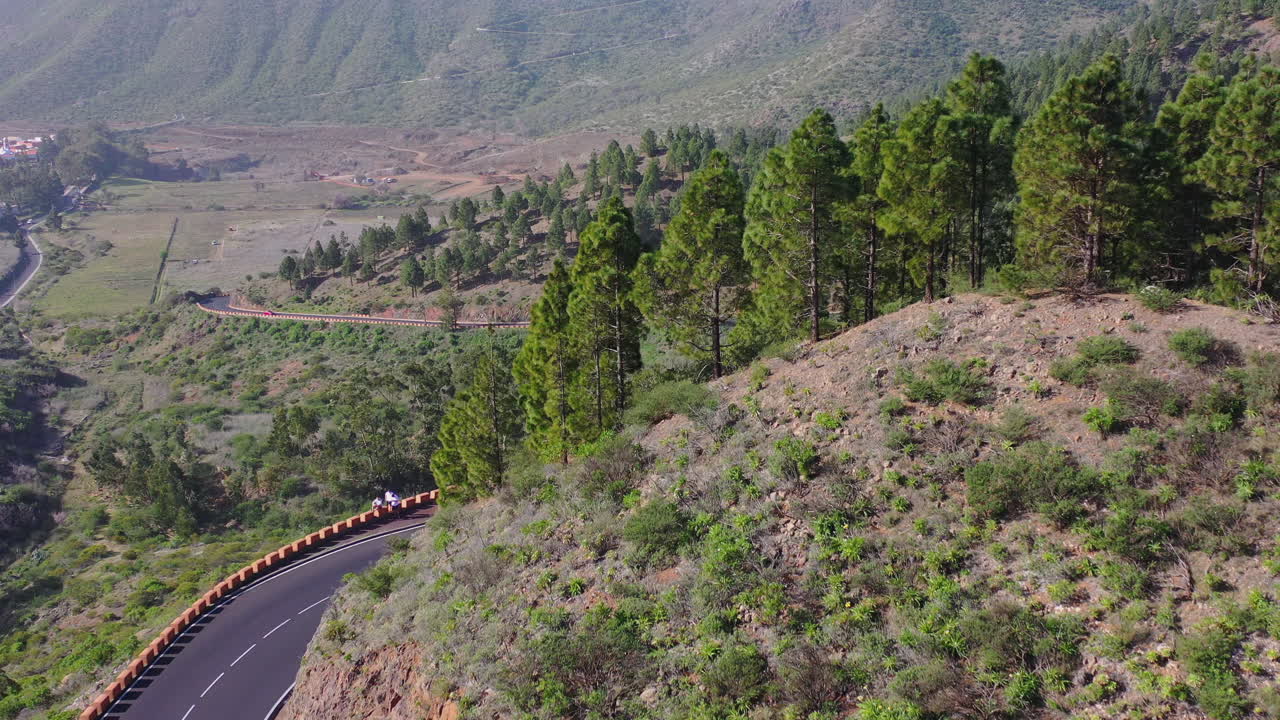 una vista de un automóvil conduciendo por una carretera de montaña de alta calidad que serpentea alrededor de una colina en una región montañosa con bosques de coníferas y arbustos en las islas canarias, españa, toma aérea en movimiento de 4k