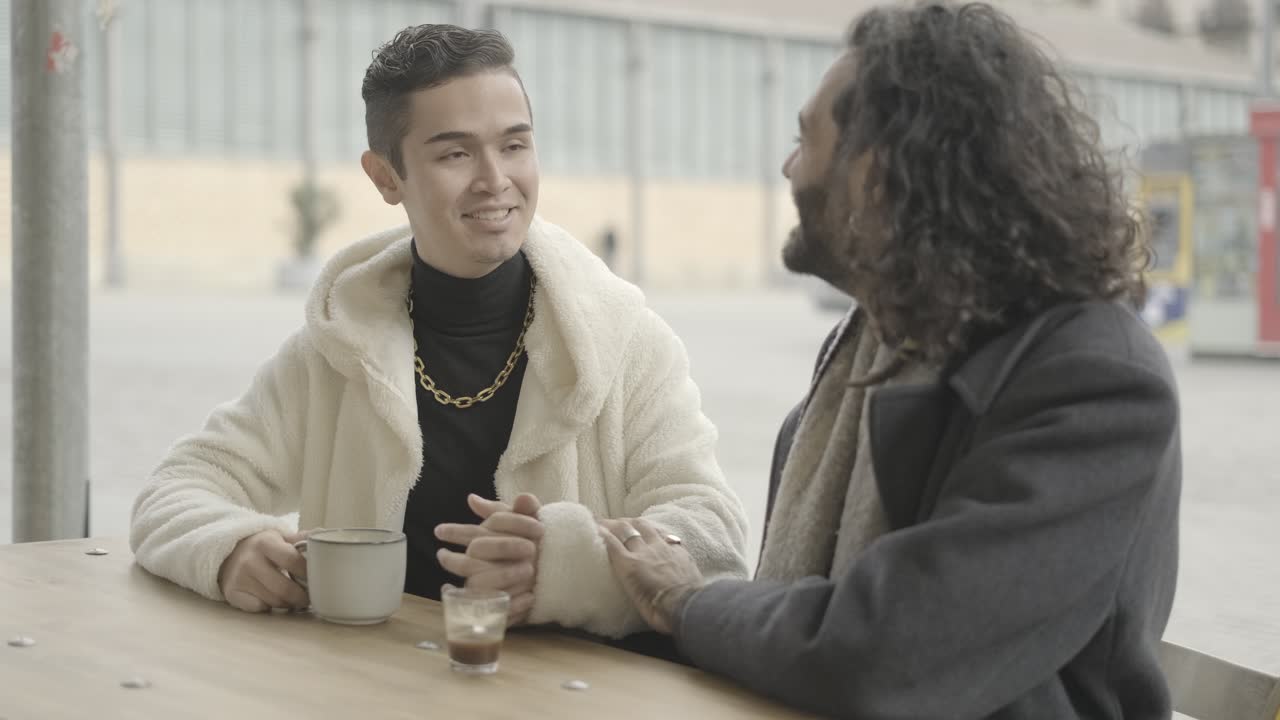 Two Men Laughing and Holding Hands at a Coffee Table