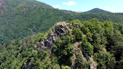 cruz de la cumbre en el acantilado rocoso y el bosque verde cubrió la cordillera