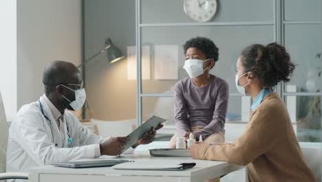 african american pediatrician in mask giving consultation to kid and his mother