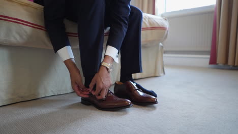 a suited man is putting on his shoes sitting in a room