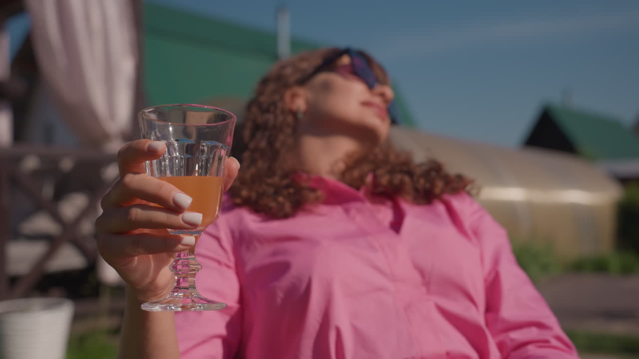 Woman With Drink, Woman In Pink Blouse Relaxing Outdoors, Casual Woman Lounging On Sunny Backyard Patio With Drink, Sunlit Backyard Scene With Woman In Pink Blouse And Playful Expression