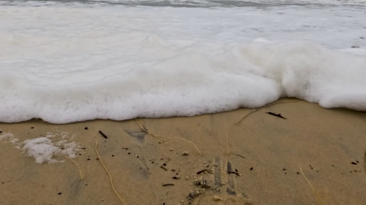 Close-up of waves creating foamy patterns on a sandy beach, highlighting the interaction between water and sand.