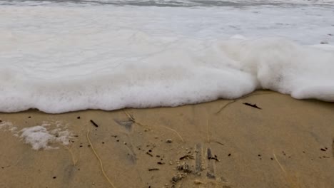 close-up of waves creating foamy patterns on a sandy beach, highlighting the interaction between water and sand.