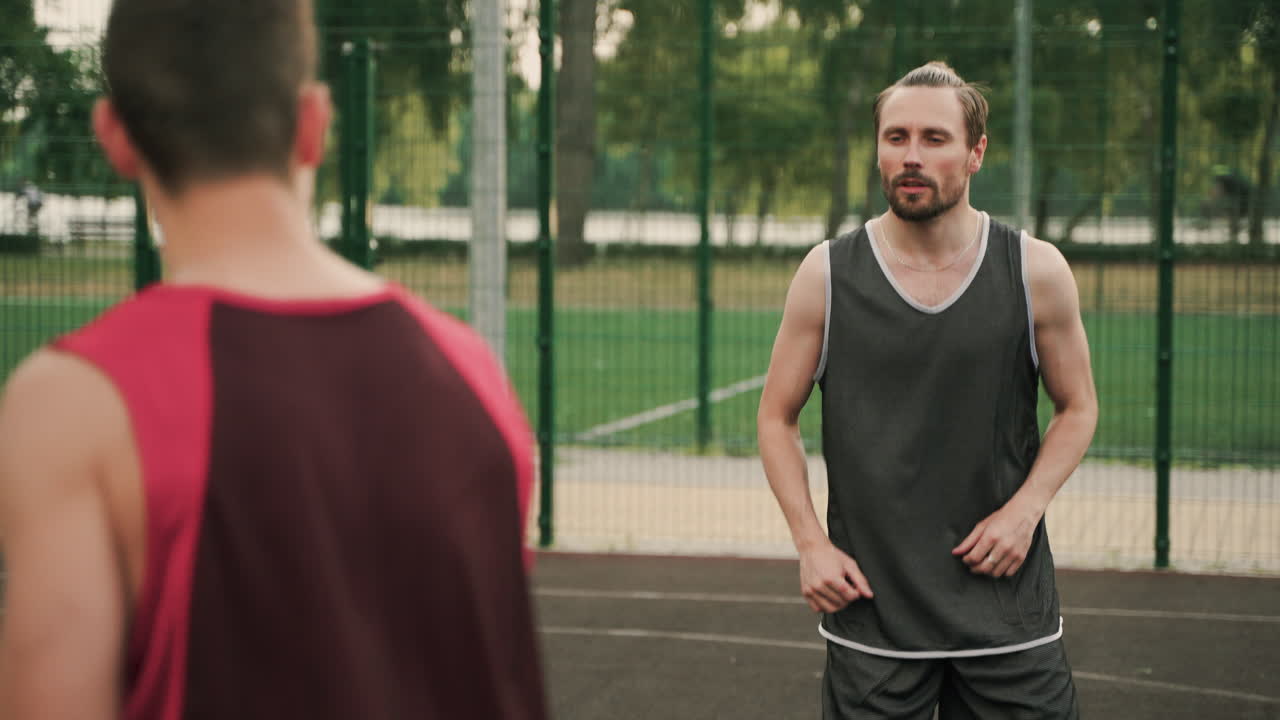dos jugadores de baloncesto masculino pasándose la pelota durante una sesión de entrenamiento en una cancha de baloncesto al aire libre