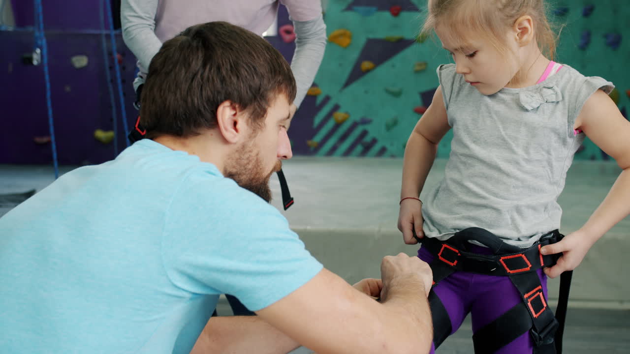 Father helping daughter put on rock climbing harness