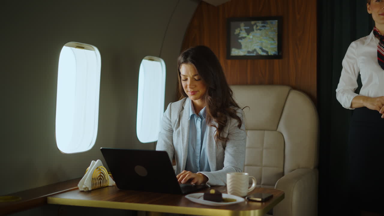 Businesswoman working on laptop in private jet with flight attendant